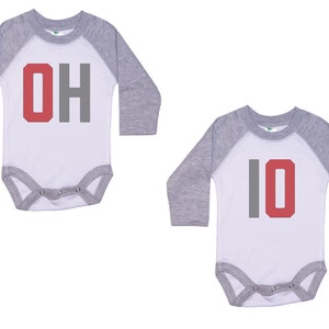 May include: Two long-sleeved baby onesies with a gray and white raglan design. One onesie has "OH" in red and gray letters. The other onesie has "10" in red and gray letters.