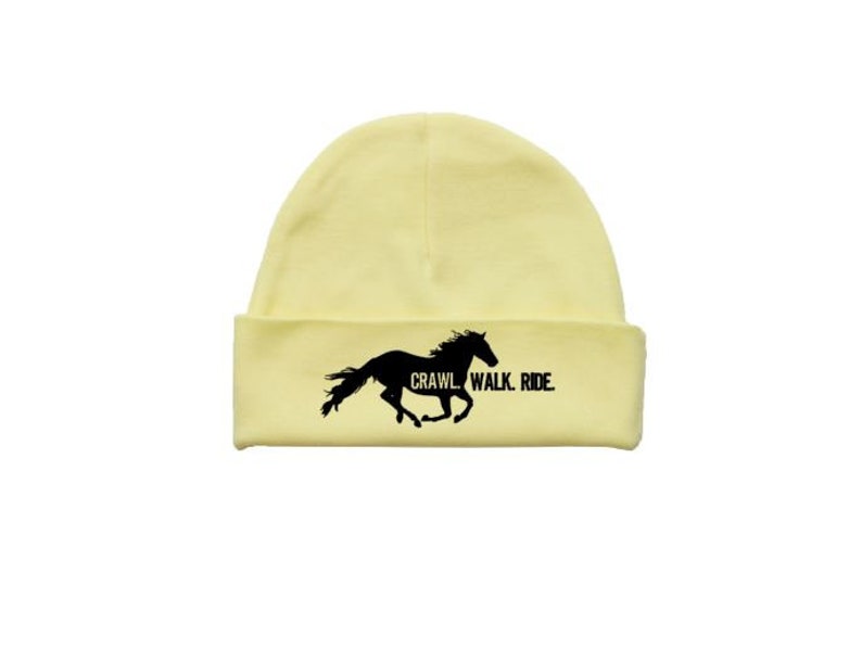 May include: A yellow beanie with a black silhouette of a horse running and the text "Crawl Walk Ride" printed on the front.