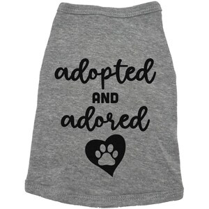 May include: Gray dog shirt with black text that says "adopted and adored" with a black paw print inside a heart.