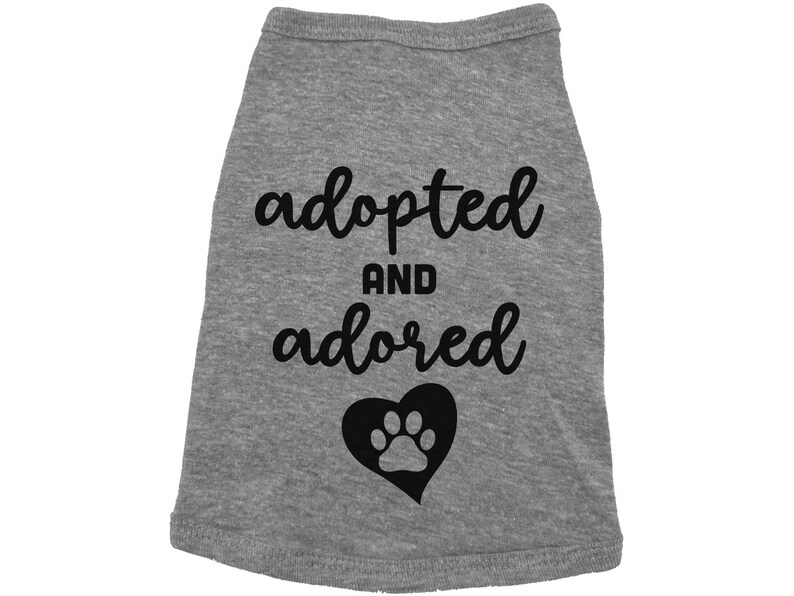 May include: Gray dog shirt with black text that says "adopted and adored" with a black paw print inside a heart.