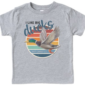 May include: A grey t-shirt with a retro-style graphic of a duck flying in front of a sunset. The text on the shirt reads "I like big ducks and I cannot lie."