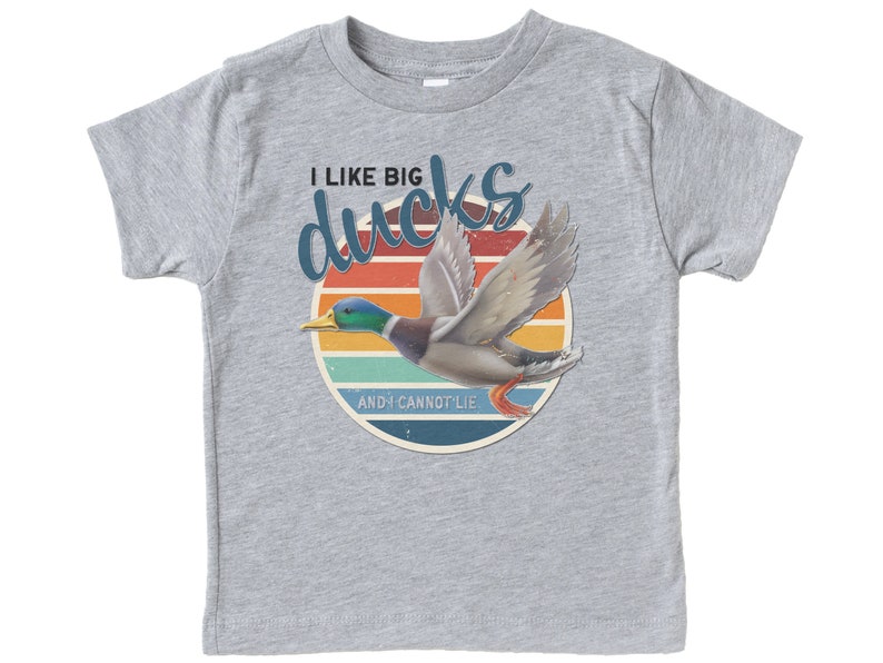 May include: A grey t-shirt with a retro-style graphic of a duck flying in front of a sunset. The text on the shirt reads "I like big ducks and I cannot lie."