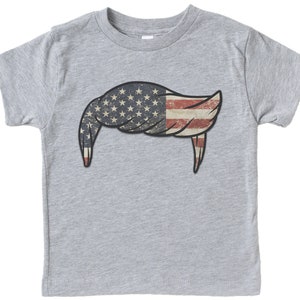 Pode incluir: Uma camiseta cinza com um design de bandeira americana vintage em forma de bigode.