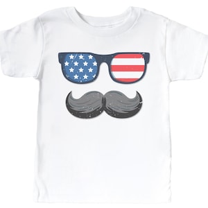 May include: White t-shirt with a graphic of sunglasses in a blue frame, one lens with stars and the other with red and white stripes, and a gray mustache. A child's tee, ideal for patriotic occasions.