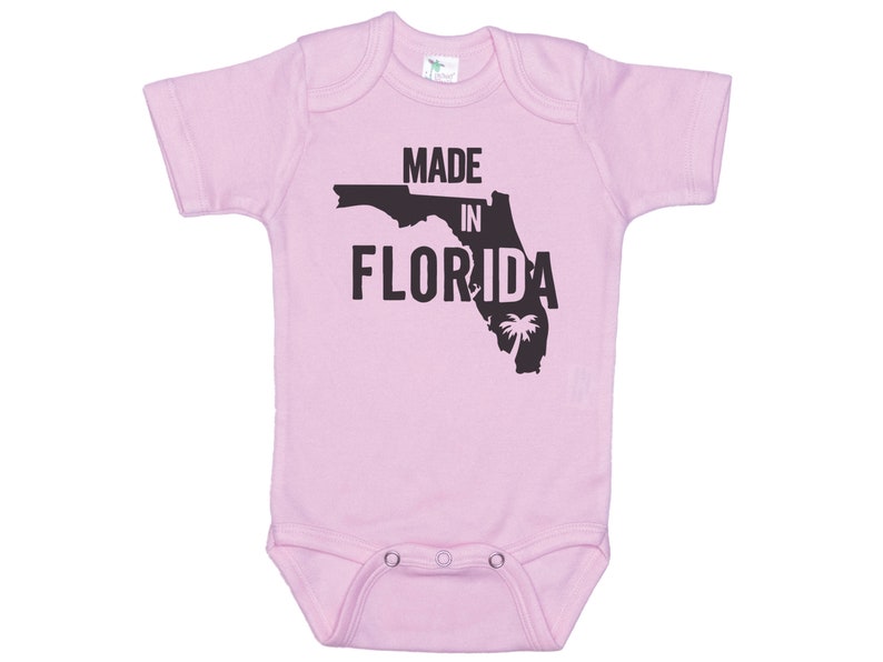 K&ouml;nnte beinhalten: Rosaer Baby-Strampler mit einer schwarzen Umrandung des Bundesstaates Florida und dem Text "Made in Florida".