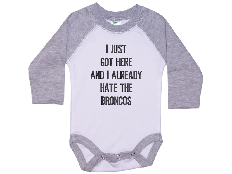 May include: A white and gray long-sleeve baby onesie with the text "I just got here and I already hate the Broncos" printed on the front.