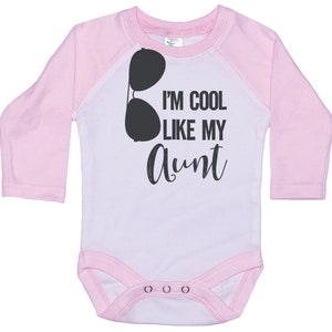 May include: Pink and white long-sleeved baby onesie with a black graphic of sunglasses and the text "I'm cool like my aunt".