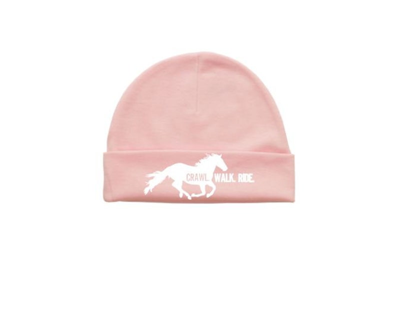 May include: A pink beanie with a white silhouette of a horse running and the text "Crawl. Walk. Ride."