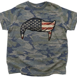 Pode incluir: Uma camiseta camuflada com um design de bandeira americana desbotada em forma de penteado.