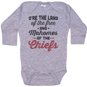 Pode incluir: Macac&atilde;o de beb&ecirc; de manga comprida cinza com o texto "O're the land of the free and Mahomes -of the- Chiefs" em preto e vermelho.
