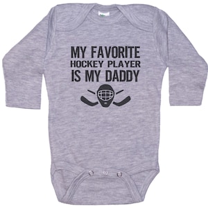 May include: Gray long-sleeve baby bodysuit with black text that reads "My favorite hockey player is my daddy" and a hockey mask with sticks.