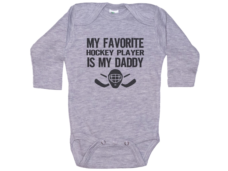May include: Gray long-sleeve baby bodysuit with black text that reads "My favorite hockey player is my daddy" and a hockey mask with sticks.