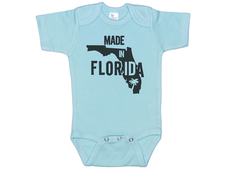 K&ouml;nnte beinhalten: Ein hellblauer Baby-Strampler mit einer schwarzen Umrandung des Bundesstaates Florida und dem Text "MADE IN FLORIDA".