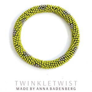 May include: A handmade bracelet with a vibrant lime green and silver beaded design. The bracelet is a circular shape, with the text "TWINKLETWIST" and "MADE BY ANNA BADENBERG" below it.