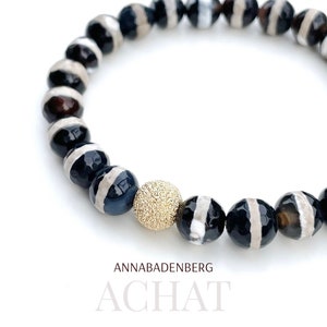 May include: A black and white agate bracelet with a gold bead charm. The bracelet is made of natural stones and has a simple, elegant design.