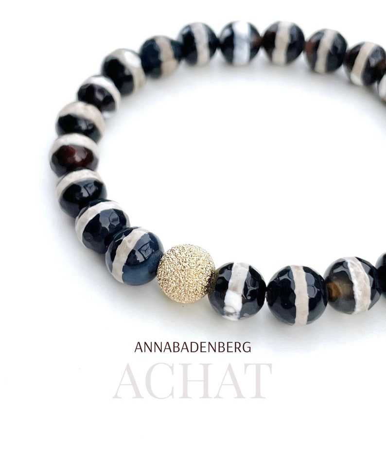 May include: A black and white agate bracelet with a gold bead charm. The bracelet is made of natural stones and has a simple, elegant design.