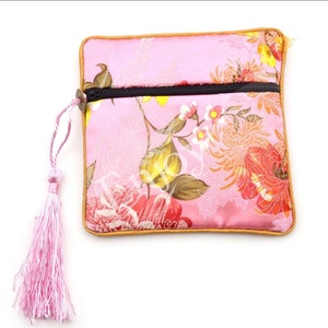 May include: A pink satin pouch with a floral print and a zipper closure. The pouch has a pink tassel attached to it.