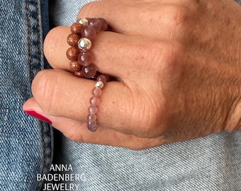 May include: Two beaded bracelets on a hand. The top bracelet is made of brown and pink beads with silver accents. The bottom bracelet is made of pink beads with silver accents.