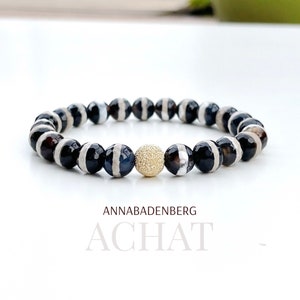 May include: Black and white agate beaded bracelet with a gold-toned spacer bead. The bracelet is made by Annabadenberg and is called "Achat".