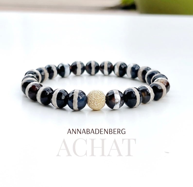 May include: Black and white agate beaded bracelet with a gold-toned spacer bead. The bracelet is made by Annabadenberg and is called "Achat".