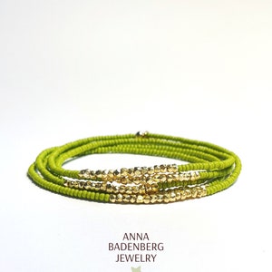 Puede incluir: Un brazalete de cuentas verdes y doradas. El brazalete está hecho de pequeñas cuentas redondas y tiene un acento dorado en el centro.