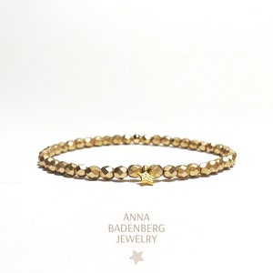 May include: A gold beaded bracelet with a small gold star charm. The bracelet is made of tiny, faceted beads.