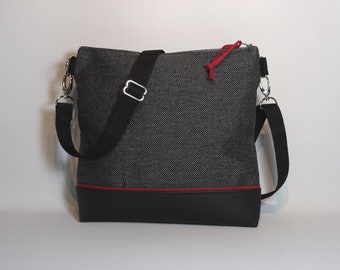 Può includere: Una borsa a tracolla nera e grigia con una zip rossa e una tracolla nera. La borsa ha un fondo in pelle nera e un bordo rosso intorno alla parte superiore.
