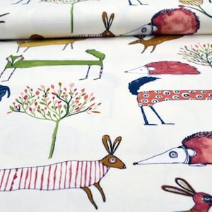 Könnte beinhalten: Weißer Stoff mit einem sich wiederholenden Muster aus stilisierten Tieren und Bäumen. Die Tiere umfassen einen Hirsch, einen Fuchs, ein Kaninchen und einen Igel. Die Bäume sind grün mit rosa Blüten. Die Tiere sind in einem skurrilen Stil mit kräftigen Farben gezeichnet.