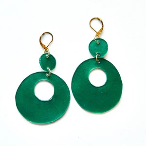 May include: A pair of green circle earrings with a smaller circle in the center of each larger circle. The earrings are connected to gold hooks.