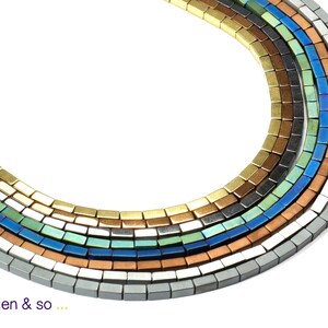Könnte beinhalten: Nahaufnahme von mehreren Strängen rechteckiger Perlen in verschiedenen Farben, darunter Gold, Bronze, Blau und Silber. Die Perlen sind in einem gebogenen Muster vor einem weißen Hintergrund angeordnet. Text unten: "Perlen & so ..."
