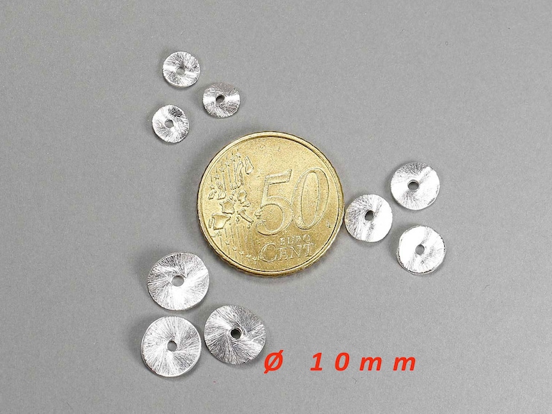 May include: A collection of small, silver-colored, disc-shaped beads with a central hole, scattered on a gray surface. A gold coin is next to the beads for size comparison. The text "&oslash; 10 mm" is in red.