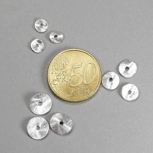 May include: A collection of small, silver-colored, disc-shaped beads with a textured surface and a central hole. A gold coin with the number 50 is next to the beads. The beads are scattered on a gray background.