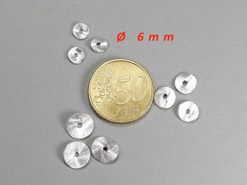 May include: A collection of small, silver-colored, circular metal beads, each with a central hole. The beads are approximately 0.24 inches in diameter. A Euro coin is included for size comparison, set against a gray background.