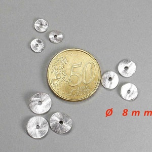May include: A collection of small, silver-colored metal discs, each with a central hole and a textured surface. The discs are approximately 0.3 inches in diameter. A gold coin is next to the discs. The text "&Oslash; 8 mm" is in red.