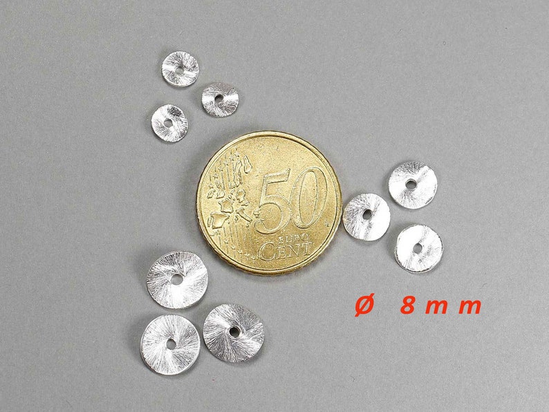 May include: A collection of small, silver-colored metal discs, each with a central hole and a textured surface. The discs are approximately 0.3 inches in diameter. A gold coin is next to the discs. The text "&Oslash; 8 mm" is in red.