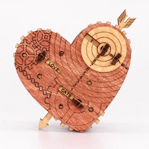 Könnte beinhalten: Ein herzförmiges Holzpuzzle mit einem Zahnrad-Design und den Wörtern "LOVE" und "CATS" eingraviert. Das Puzzle hat ein drehbares Zifferblatt mit den Zahlen 1 bis 10 und einen Pfeil, der nach rechts zeigt.
