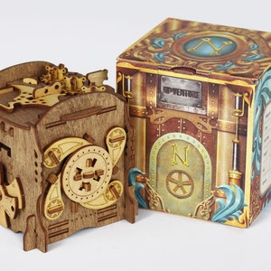 Könnte beinhalten: Eine Holzkästchen-Rätselbox mit komplizierten Zahnrädern und einem Kompass-Design. Die Box ist geschlossen und hat ein braunes und beigefarbenes Farbschema. Die Box befindet sich neben einer Pappbox mit einem ähnlichen Design und dem aufgedruckten Wort "Adventure".