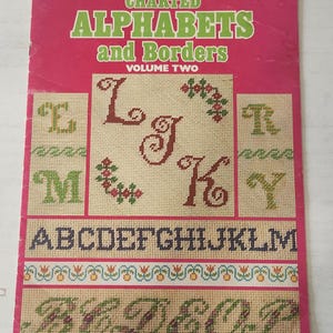 Puede incluir: Un libro de manualidades vintage titulado "Charted Alphabets and Borders, Volume Two" de Leisure Arts. La portada es rosa con diseños de alfabeto y bordes en punto de cruz verde y marrón. El folleto está marcado con el número 57.