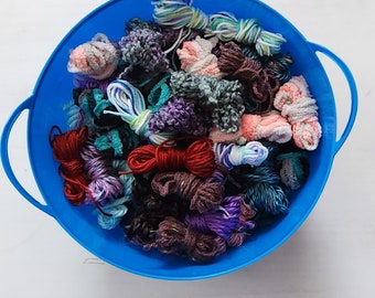May include: A blue plastic bowl filled with a variety of colorful yarn scraps. The yarn is in different colors, including pink, purple, blue, green, red, and brown.