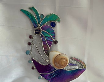 Könnte beinhalten: Ein Kunstwerk aus Glasmalerei mit einer Muschel aus schillerndem violettem, blauem und grünem Glas. Das Stück ist auf einem weißen Hintergrund montiert.