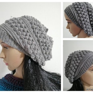 Könnte beinhalten: Graue Häkelmütze mit strukturiertem, noppenförmigem Design. Die Mütze wird auf einem Mannequin-Kopf mit langen schwarzen Haaren gezeigt.
