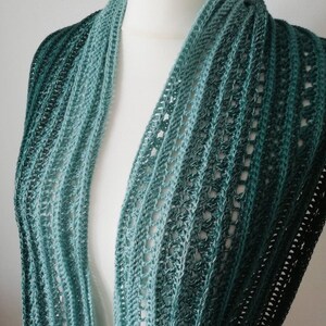 May include: A teal and green ombre crochet scarf with a lacy pattern. The scarf is draped over a white mannequin.