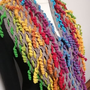 May include: A colourful crochet scarf with a rainbow pattern. The scarf is made with a variety of colours, including red, orange, yellow, green, blue, and purple. The scarf is crocheted in a loose, open stitch, which gives it a light and airy feel.