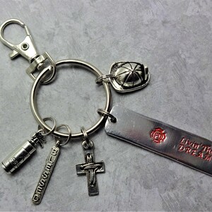 May include: Silver keychain with multiple charms, including a firefighter's helmet, a fire extinguisher, a cross, and a tag that says "Blessed". A rectangular tag with the text "Livin' The DREAM" and a FD logo is also included.