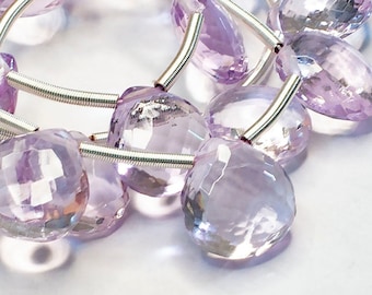 May include: A strand of pale lavender amethyst gemstone beads, each bead is faceted and has a teardrop shape. The beads are strung on a silver wire.