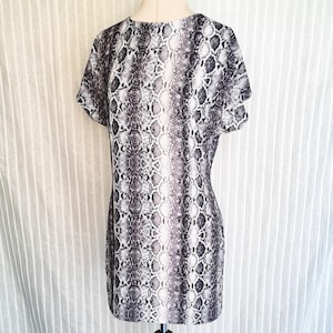 Puede incluir: Un vestido de manga corta con estampado de piel de serpiente en tonos grises y blancos. El vestido es entallado y tiene un escote redondo.