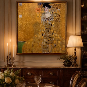 Puede incluir: Un cuadro enmarcado de una mujer con un vestido dorado, con un sombrero negro, cuelga sobre un aparador de madera. La pintura tiene un fondo dorado con patrones geométricos. Una lámpara encendida y velas están a ambos lados de la pintura. Una mesa de comedor está puesta.