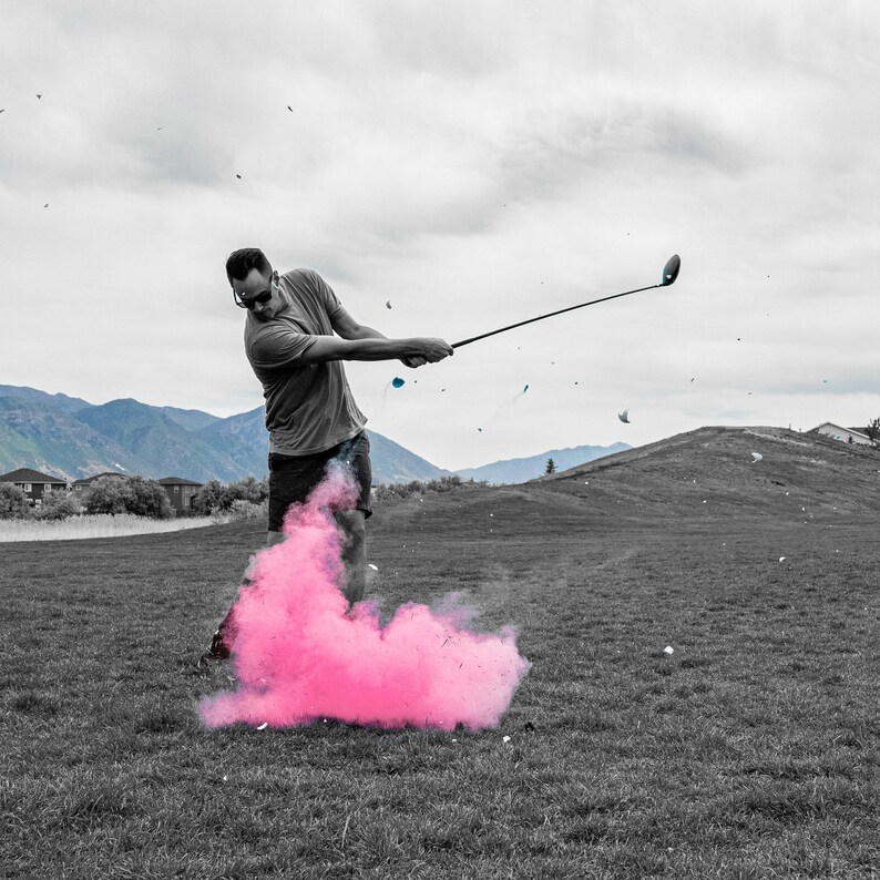 May include: A person wearing black and white clothing swings a golf club, producing a pink cloud of smoke behind them.