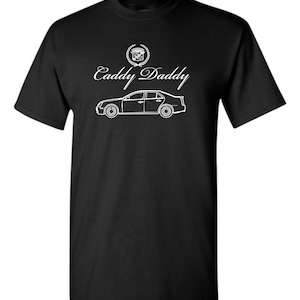 May include: Black t-shirt with a white outline of a Cadillac car and the text "Caddy Daddy" with a Cadillac logo above the text.
