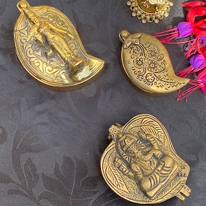 Op de afbeelding: Drie gouden metalen doosjes met ingewikkelde ontwerpen. De doosjes zijn bladvormig en hebben reliëfbeelden van hindoeïstische goden.